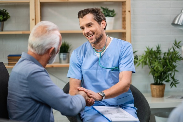 Carreiras mais bem pagas do Brasil - Feliz clínico geral conversando com um homem sênior enquanto aperta a mão dele durante uma visita domiciliar