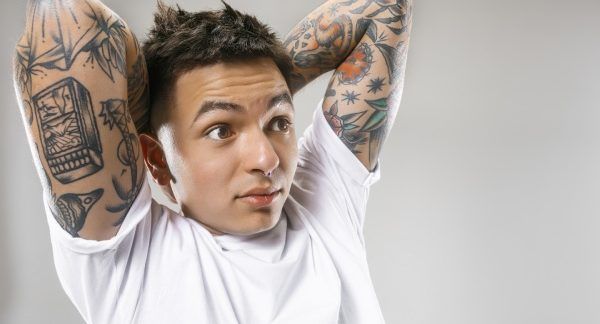 melhores centros de remoção de tatuagens - Um homem com as mãos cruzadas atrás do pescoço, exibindo as tatuagens em seu braço.